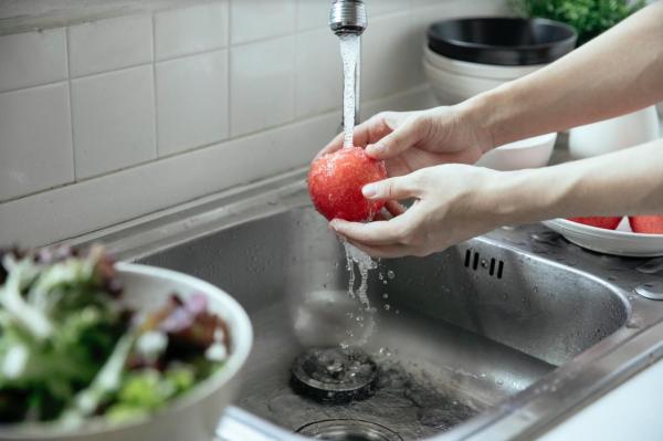 A person washing an apple in the kitchen sink and trying to avoid water waste, as it is one of the ways your house is draining your bank account